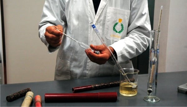 Technician in white coat and Casalvento Laboratories company logo measuring the density of an essential oil with a special hydrometer