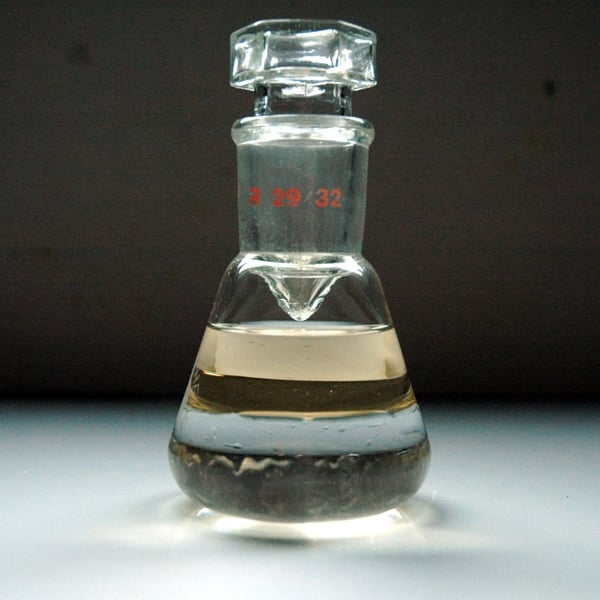 Laboratory flask in borosilicate containing absolute essence of Rosa damascena produced by Casalvento on a two-tone light gray and dark gray background