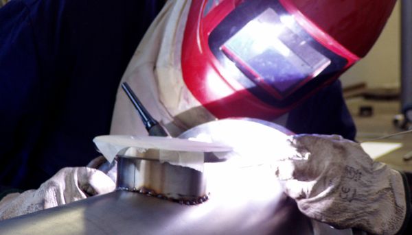 Worker with red mask for TIG welding of stainless steel elements of an essential oil distiller