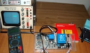 Schede elettroniche con oscilloscopio e multimetro digitale per il controllo dei parametri della distillazione, cavi di connessione alle sonde di misura nella scatola rossa Honeywell su un piano di legno