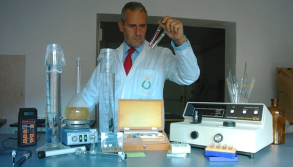 Il dottor Lorenzo Domini in camice e cravatta rossa nei Laboratori Casalvento con cilindri graduati, agitatori magnetici e spettrofotometri per la misura della assorbanza e trasmittanza di un olio essenziale