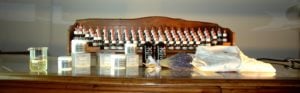 Vasetti di crema cosmetica e flaconi farmaceutici di oli essenziali con tappo bianco e rosso, camice da medico ripiegato e stetoscopio su un piano di vetro
