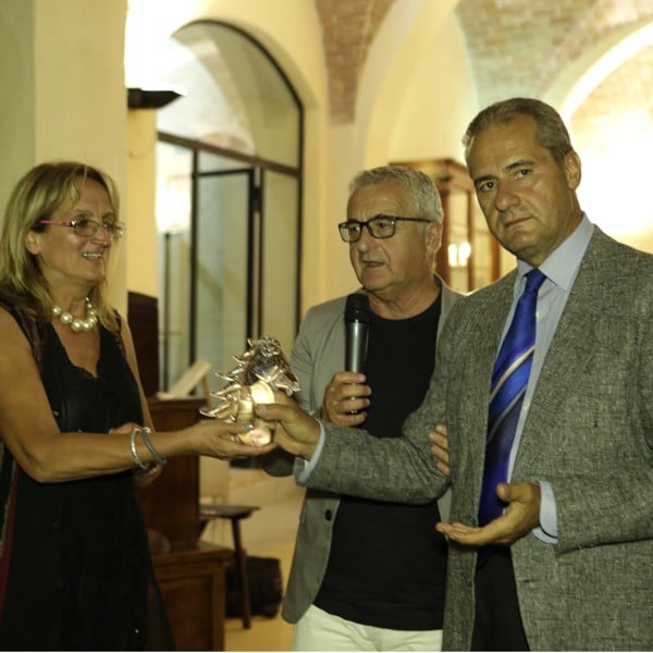 Image of the award ceremony of Lorenzo Domini in a gray jacket with a crystal horse for innovation in Chianti and Valdelsa of the Casalvento Laboratories in the presence of the mayor of Casole D'Elsa