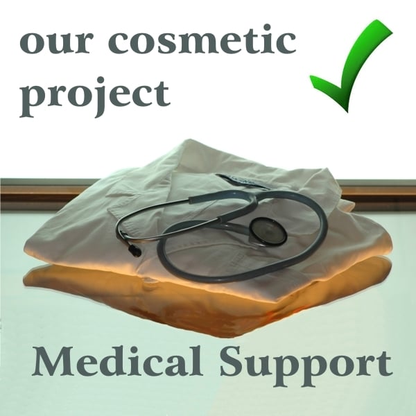 White coat folded and placed on a glass lit from below, stethoscope placed on top and black writing: our cosmetic project, medical support. Green check mark