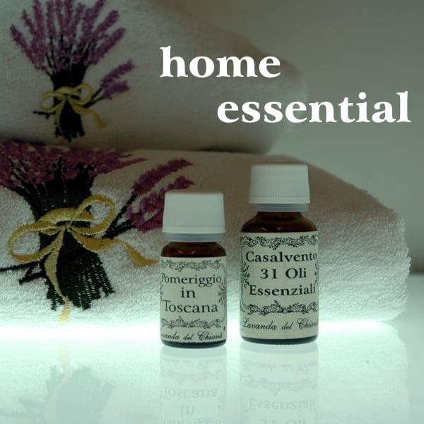 Yellow glass bottles and white cap with cream-coloured label with the words Casalvento 31 oils and Afternoon in Tuscany on the background of a sponge towel and a colored bouquet of blue lavender flowers with the words: home essential