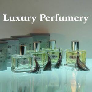Four bottles of perfume Ochra, Oblio, Grise and Jaras in transparent glass with silver cap and pendant with silver box in the background in light color, reflections on the glass on the support in white writing: luxury perfumery