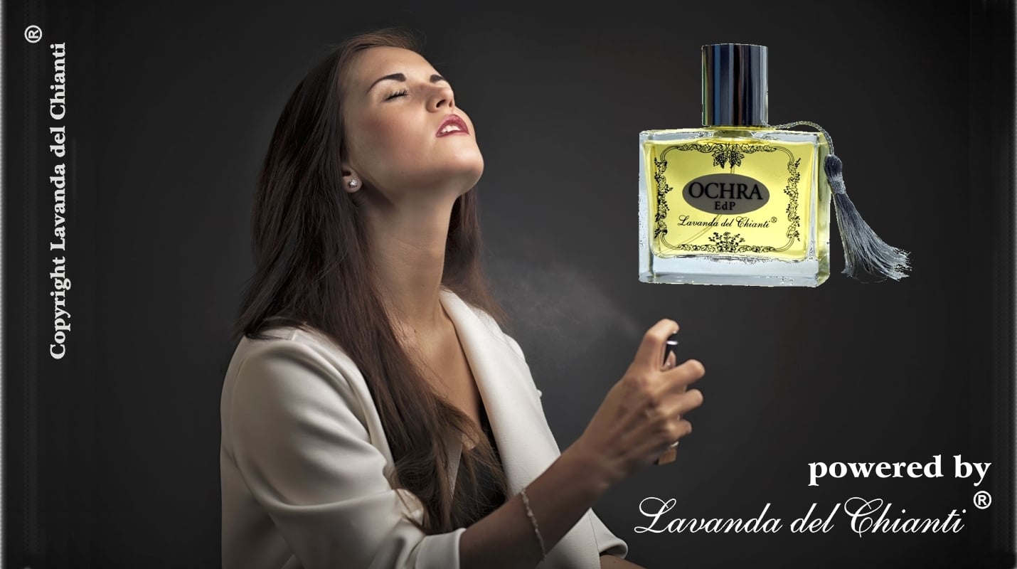 Beautiful young woman with brown hair spraying perfume on her neck against black background top right Ochra perfume bottle; white characters: copyright Lavanda del Chianti and powered by Lavanda del Chianti