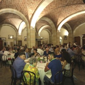 Immagine di una sala da pranzo con archi a soffitto di una cena conviviale di oltre 100 invitati seduti a tavoli rotondi con la presenza delle autorità