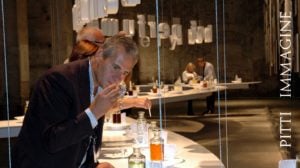 Lorenzo Domini prova una miscela profumata a Fragranze su tavolo bianco in ampia sala marrone